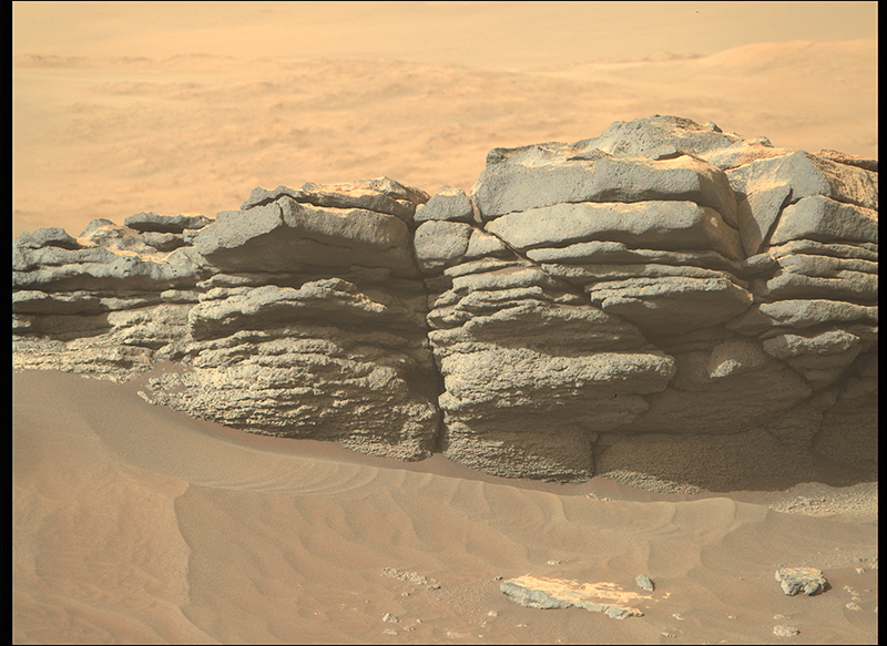 Reddish brown rocks stick out of red sands stretching into the distance on Mars.