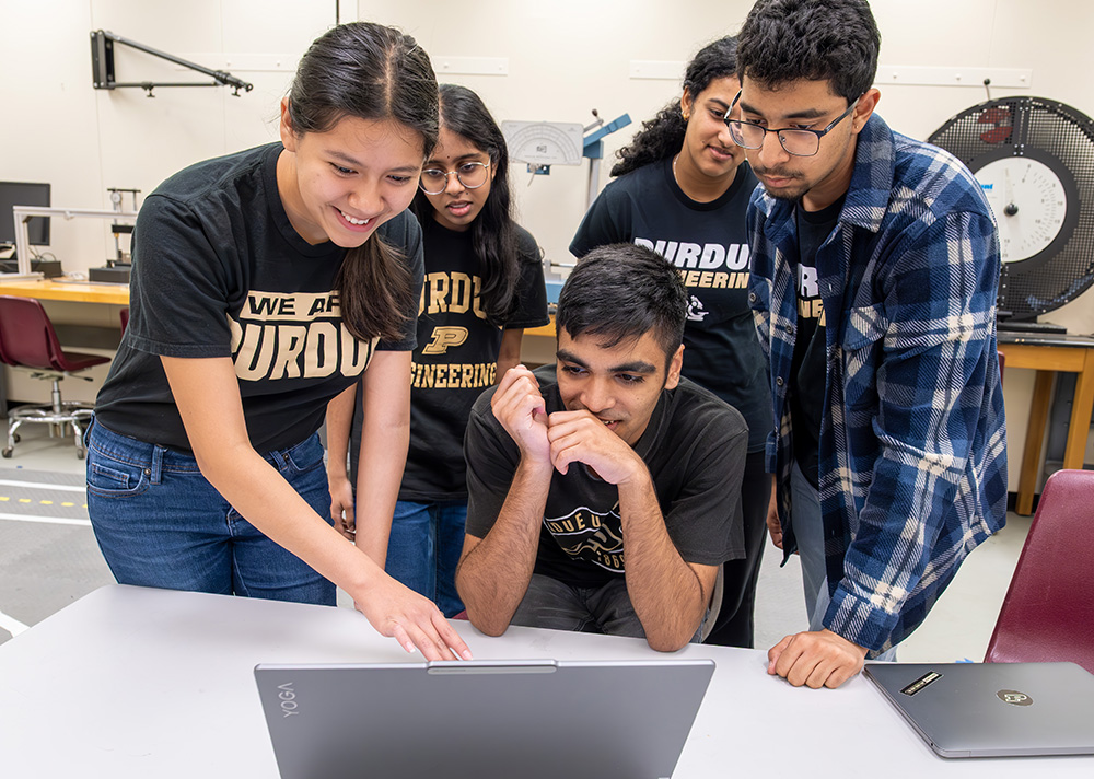 A group of students gather around a laptop.