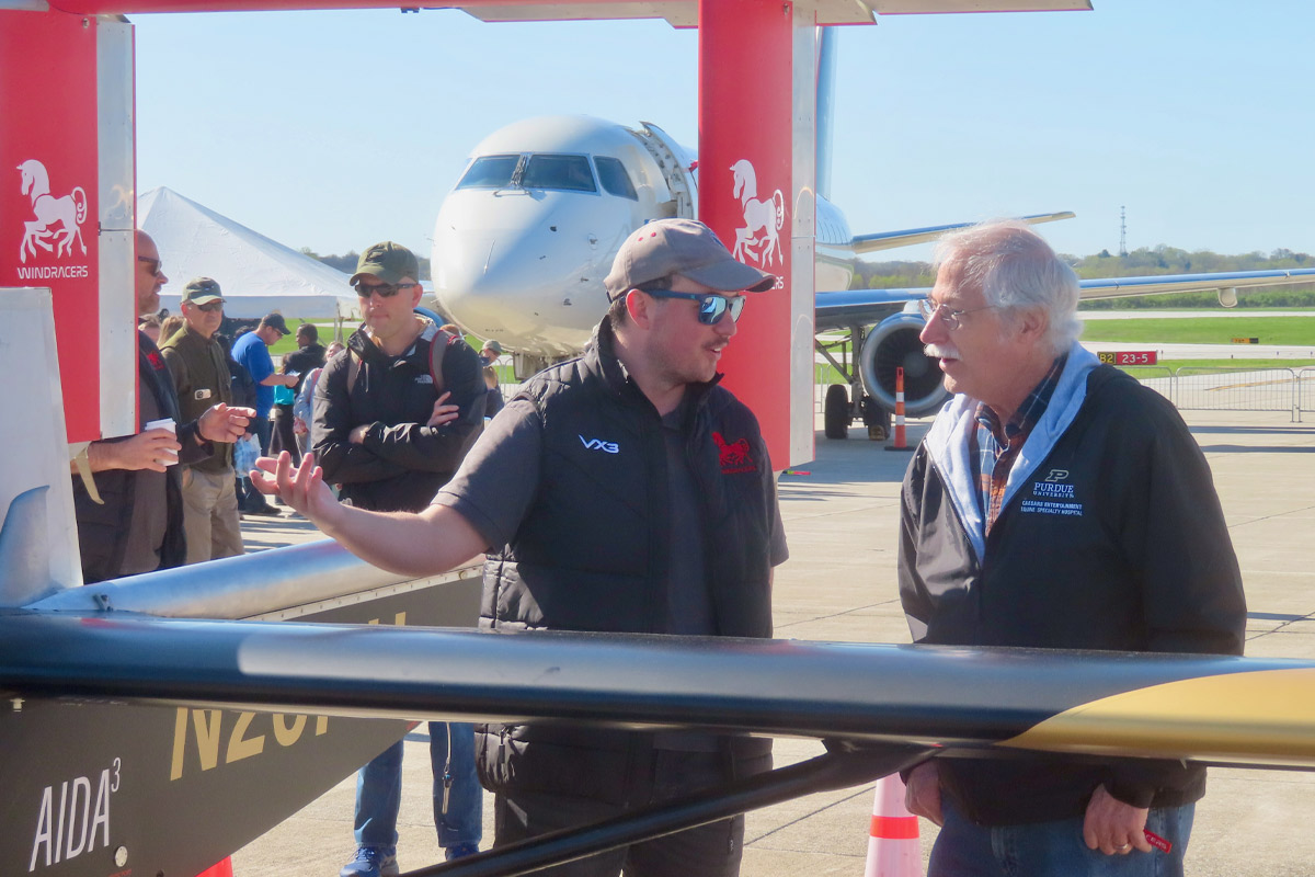 A photo of an aviation day participant talking to a visitor about airplanes  