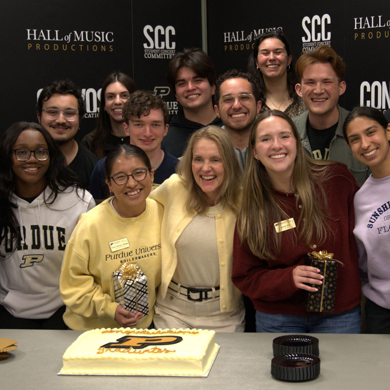 Purdue students with Beth McCuskey, smiling around a Purdue-themed cake.