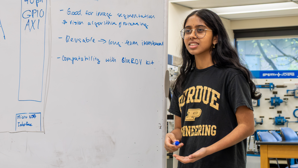 A young Purdue Engineering woman giving a presentation next to a whiteboard