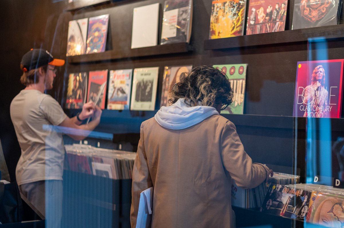 Students looking through vinyl records in front of a wall displaying several records.