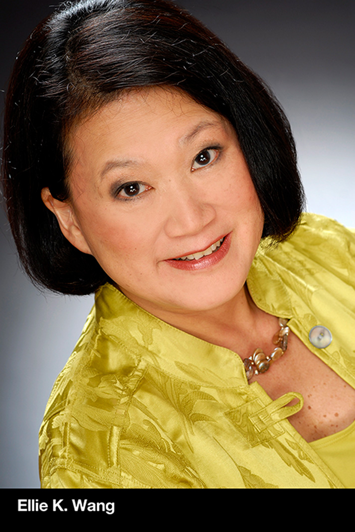 Professional headshot of Ellie K. Wang, wearing a patterned yellow jacket and necklace, smiling at the camera against a dark gradient background.
