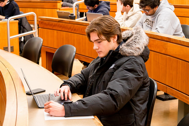 A student sits in a classroom looking at his laptop